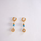 Pair of gold earrings with blue evil eye charms on a white background
