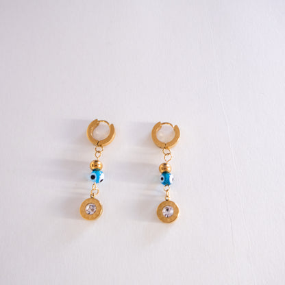 Pair of gold earrings with blue evil eye charms on a white background