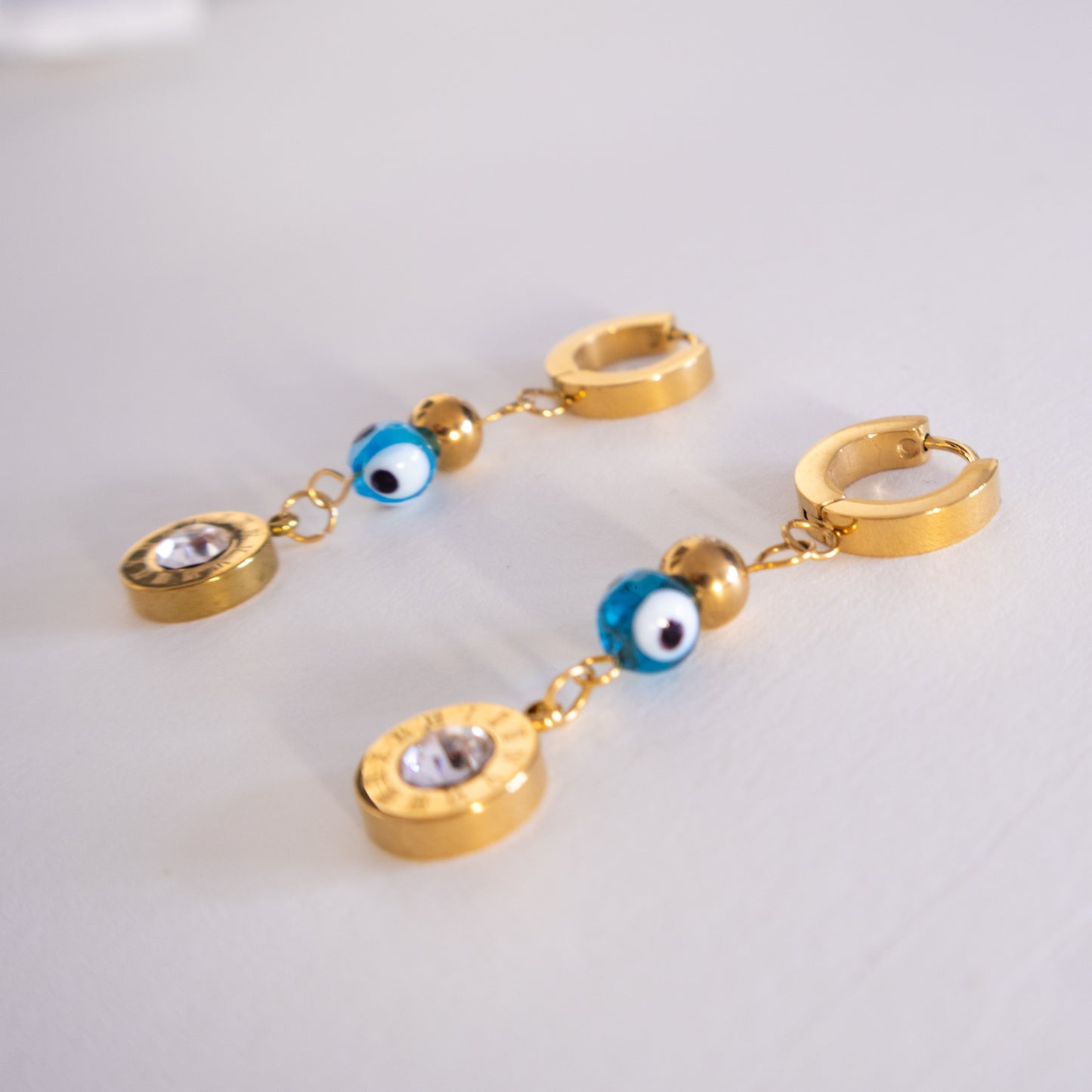 Gold hoop earrings with blue evil eye charms on a light gray background