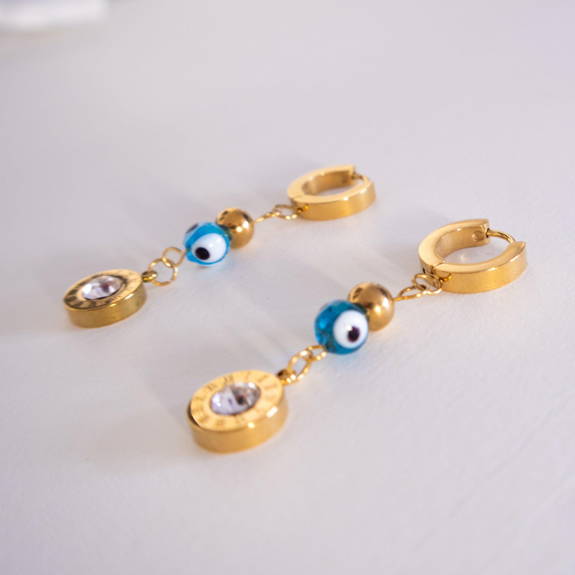 Gold hoop earrings with blue evil eye charms on a light gray background