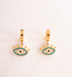 Gold hoop earrings with eye design on a light pink background