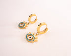 Gold earrings with eye design on a light pink background