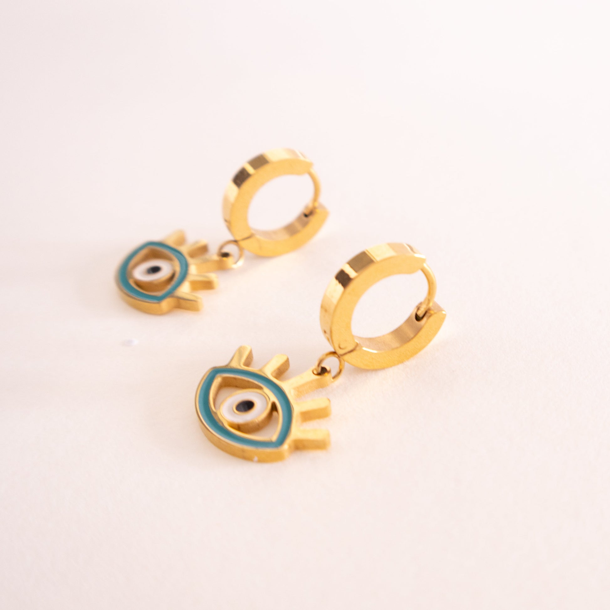 Gold earrings with eye design on a light pink background