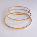 Three gold bangles stacked on a white background