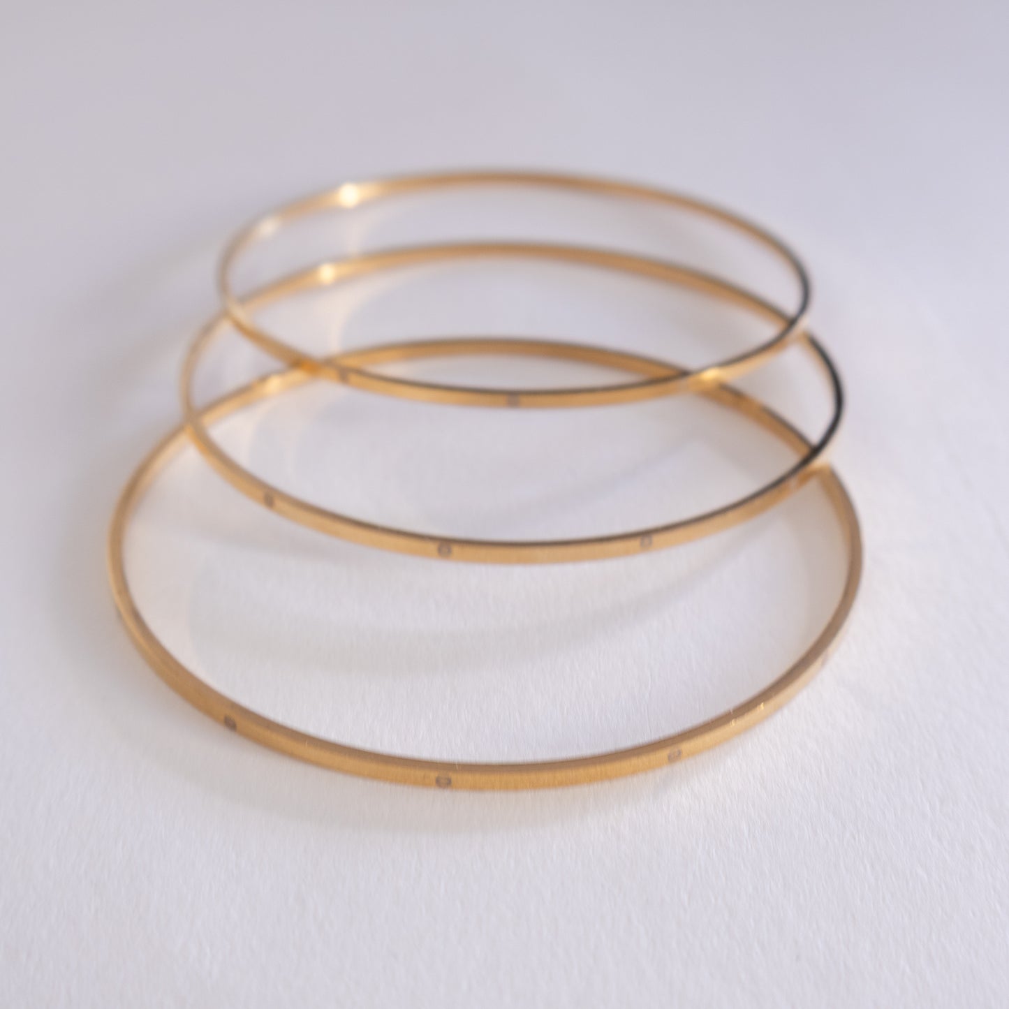 Three gold bangles stacked on a white background