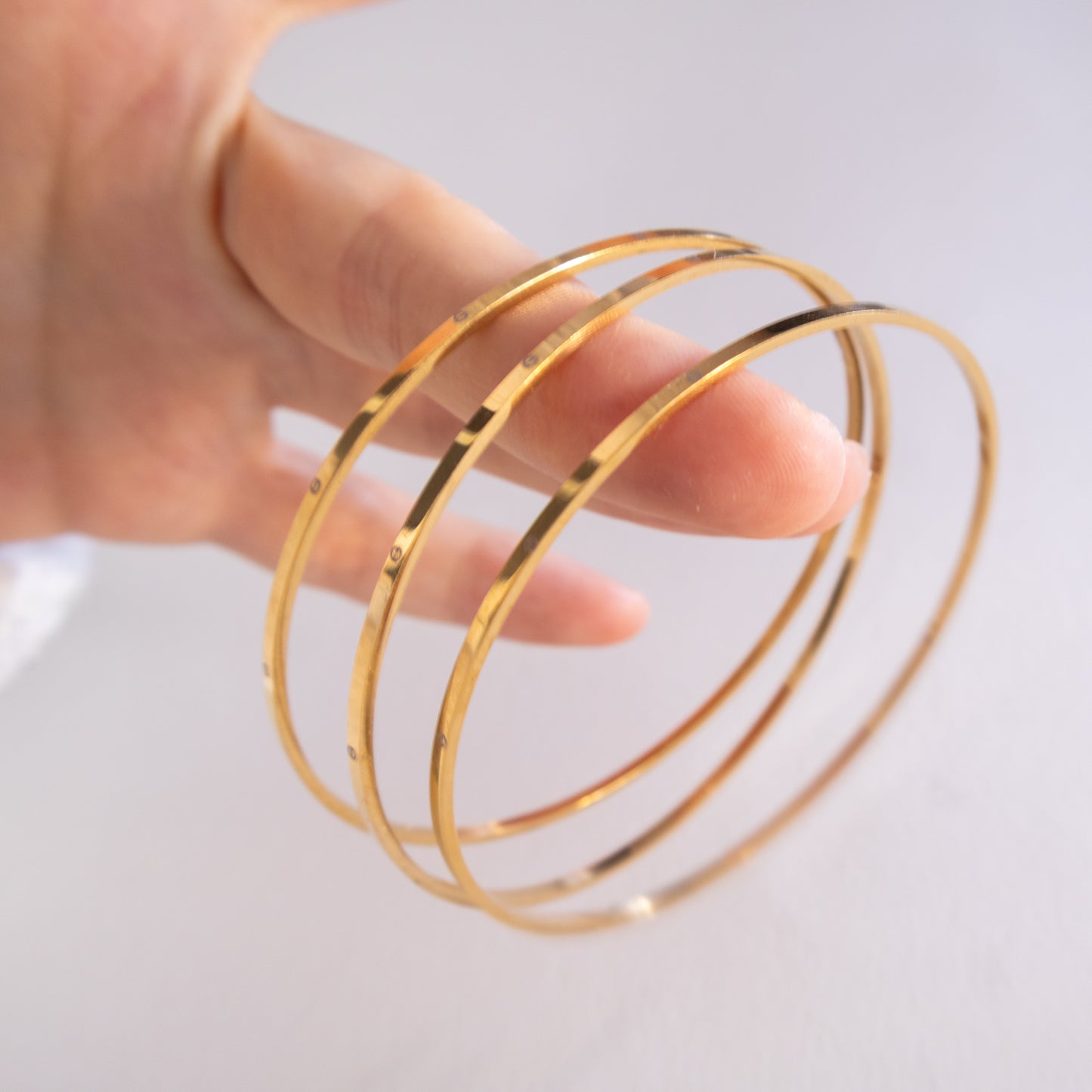 Gold bangles on a hand against a light background
