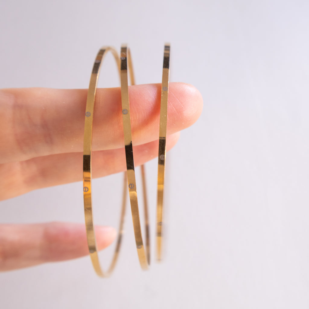 Gold hoop earrings held between fingers against a light background