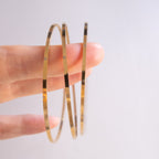 Gold hoop earrings held between fingers against a light background