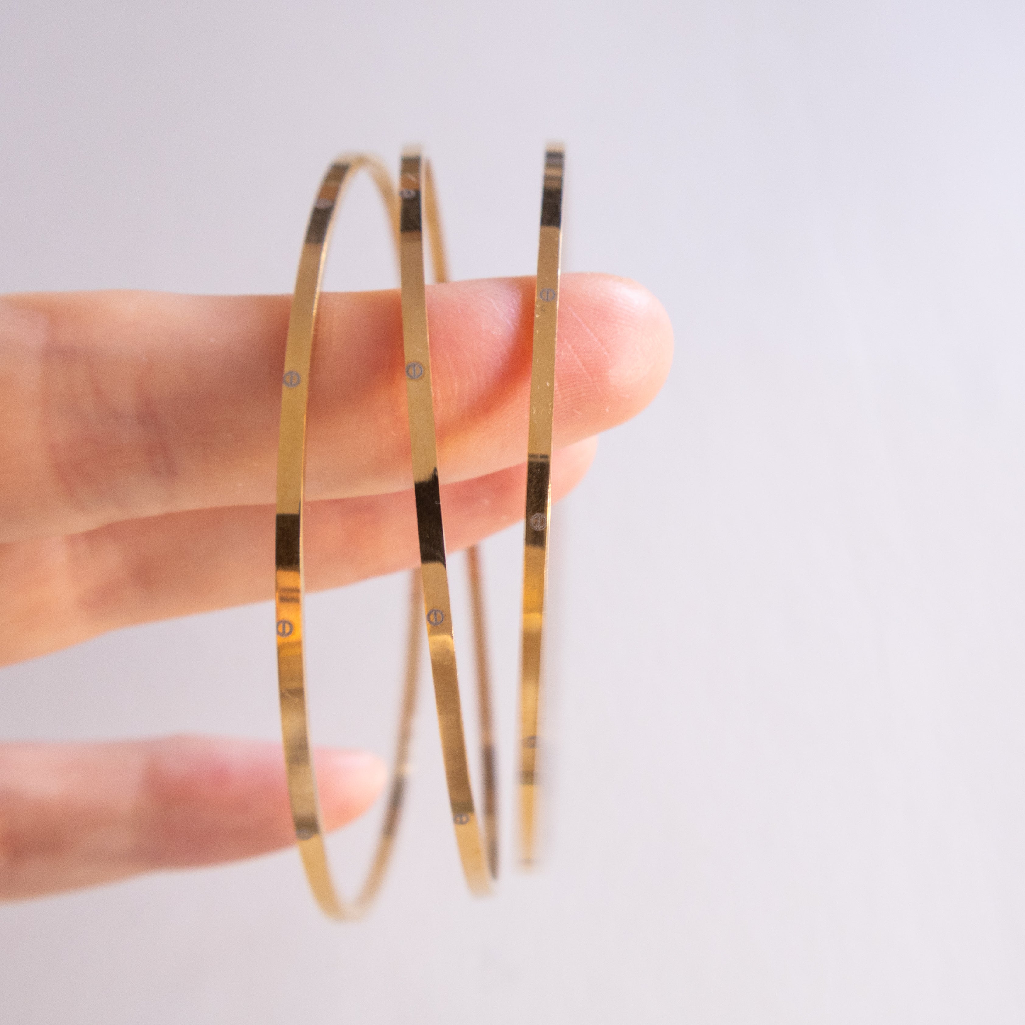Gold hoop earrings held between fingers against a light background