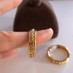 Gold ring with intricate design worn on a finger, with another ring on a white surface.