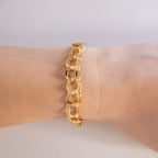 Gold chain bracelet on a wrist against a neutral background
