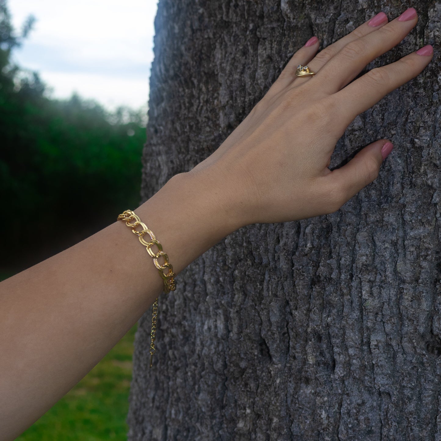Hand with gold bracelet and ring on a tree trunk
