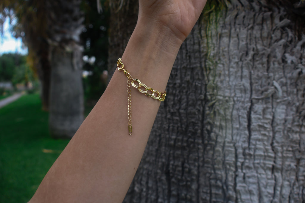 Gold chain bracelet on a wrist with a blurred natural background