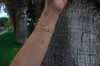Gold chain bracelet on a wrist with a blurred natural background