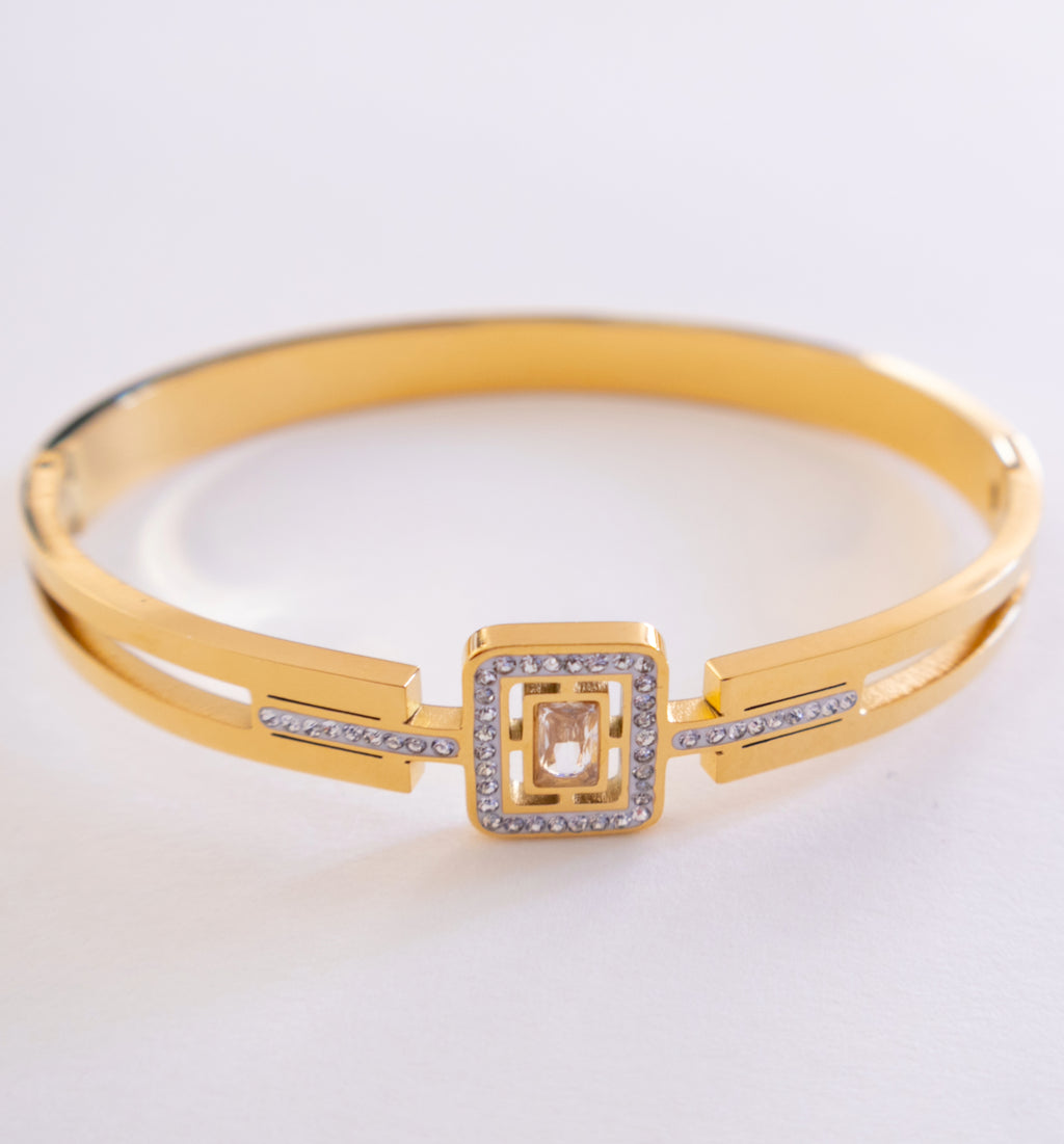 Gold bracelet with a square design and clear stones on a light gray background