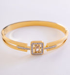 Gold bracelet with a square design and clear stones on a light gray background