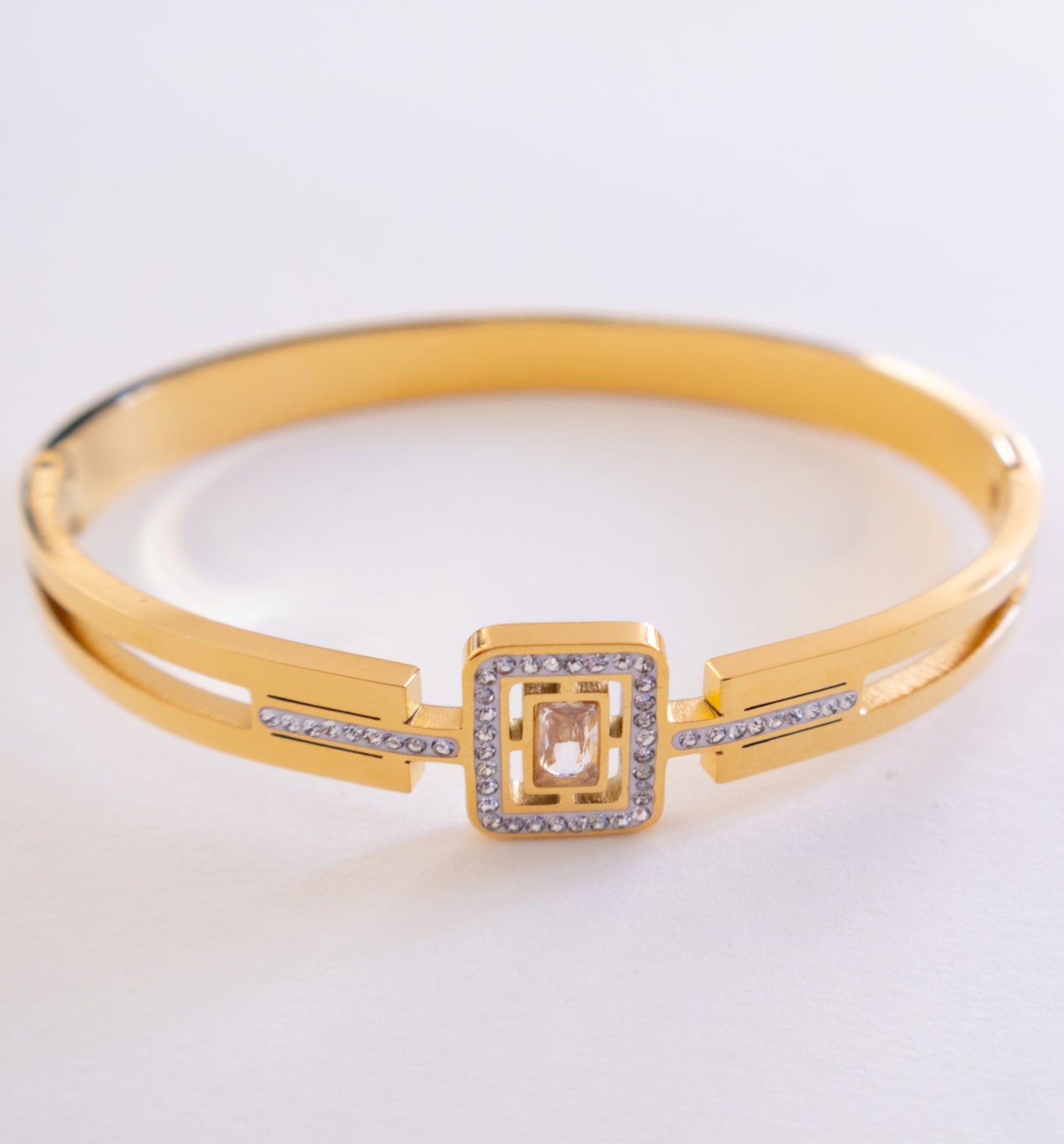 Gold bracelet with a square design and clear stones on a light gray background