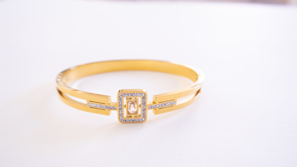 Gold bracelet with a square clasp on a white background