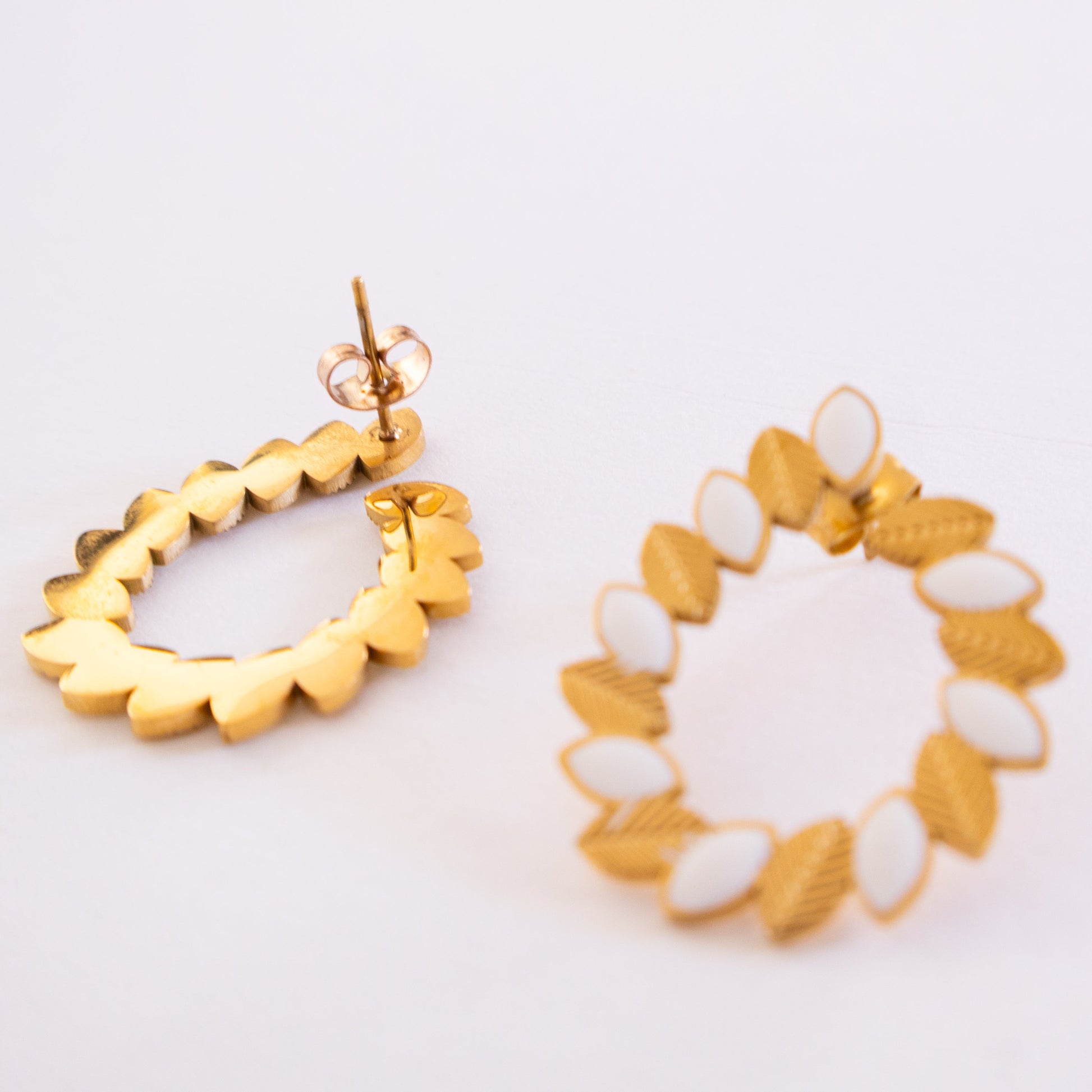 Gold and white earrings on a light background