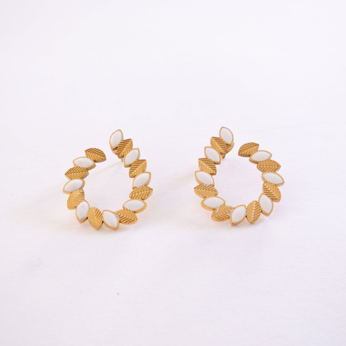 Pair of gold and white hoop earrings on a light gray background
