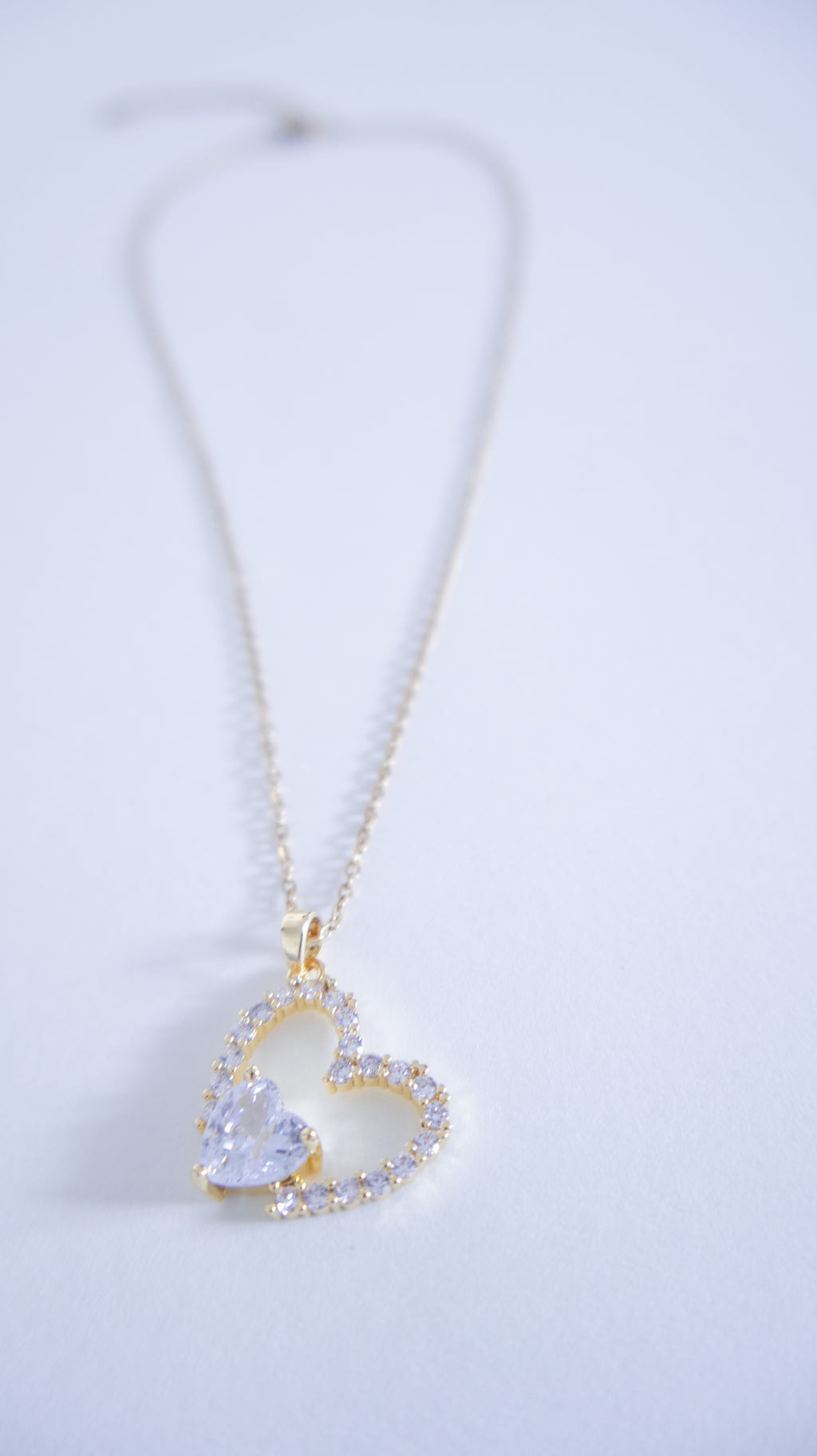 Heart-shaped necklace with a clear gemstone on a light gray background