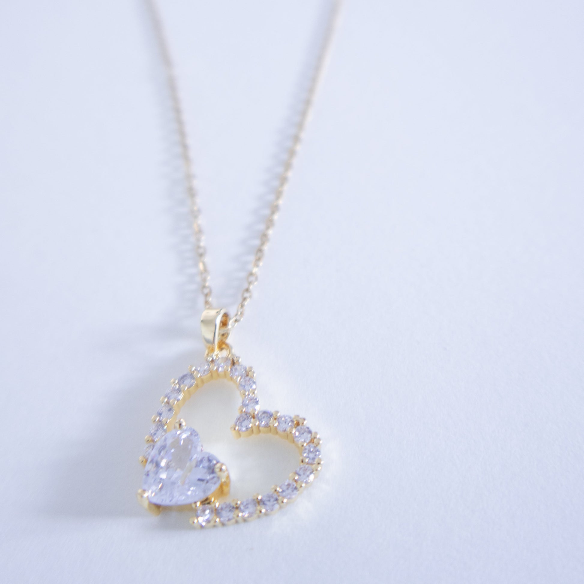 Heart-shaped necklace with a clear gemstone on a light gray background