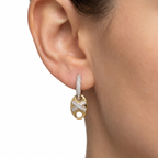 Gold and silver earring worn on an ear with a plain background