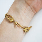 Gold bracelet with a heart charm on a wrist against a white background