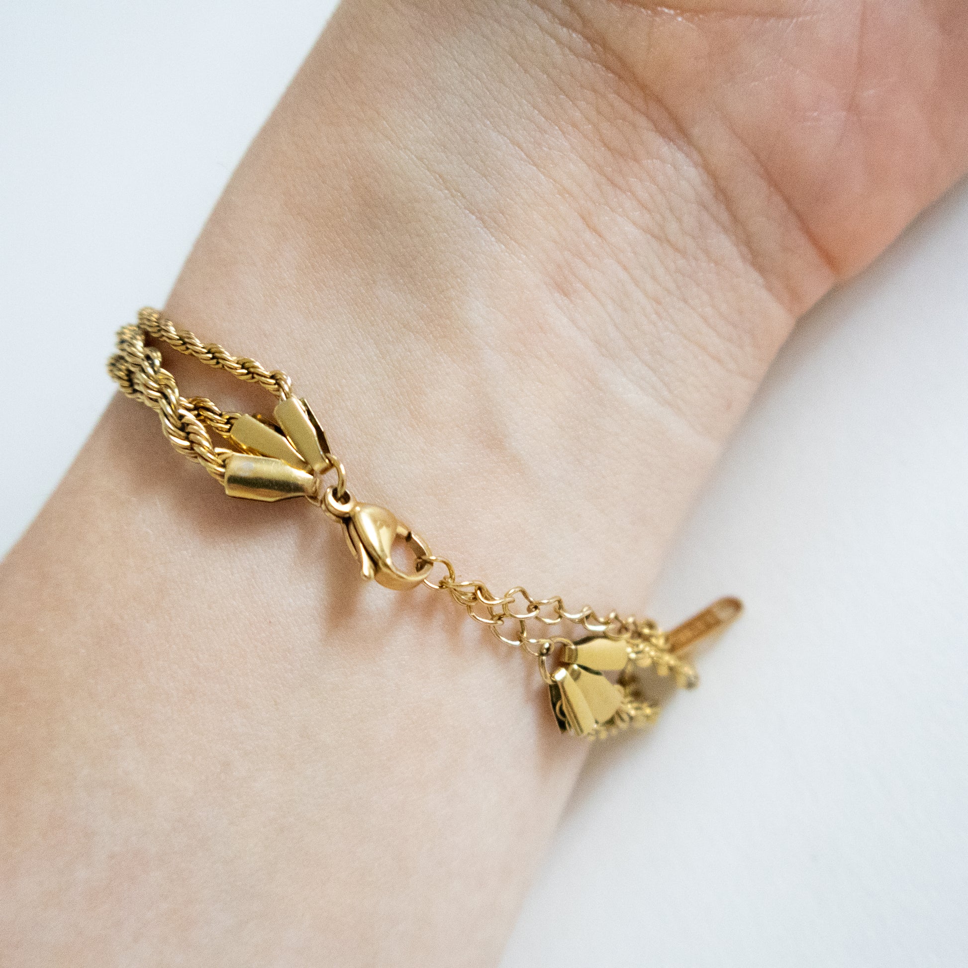 Gold bracelet with a heart charm on a wrist against a white background
