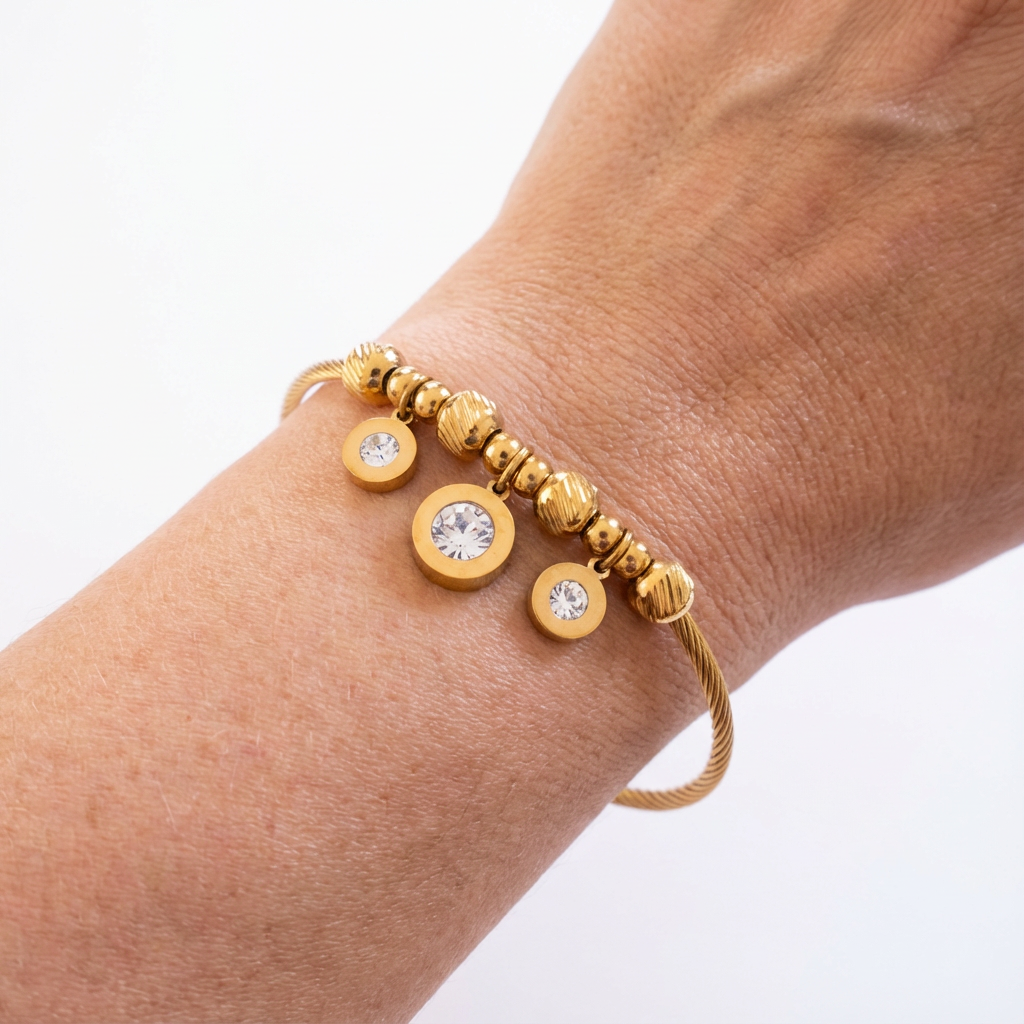 Gold bracelet with circular beads and crystals on a wrist against a white background