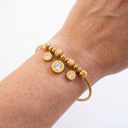 Gold bracelet with circular beads and crystals on a wrist against a white background