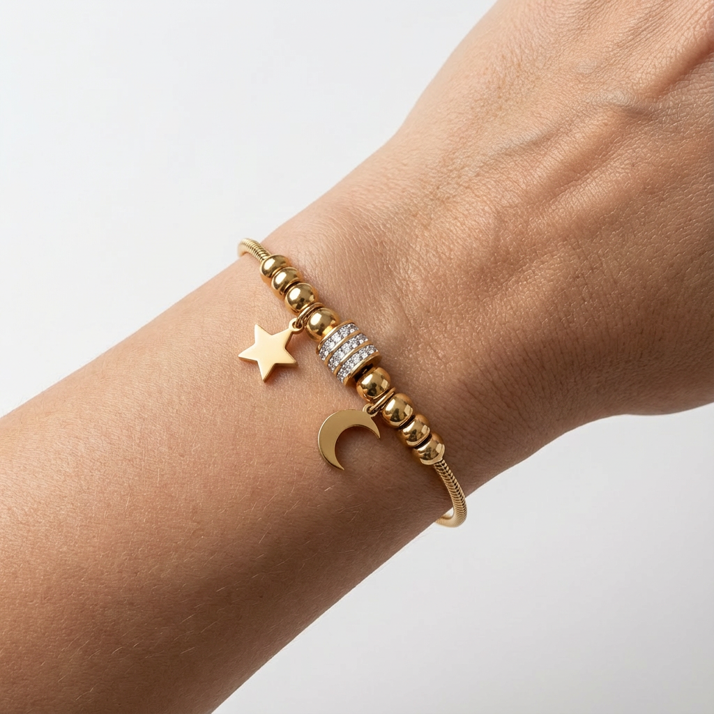 Gold bracelet with star and moon charm on a wrist against a light background