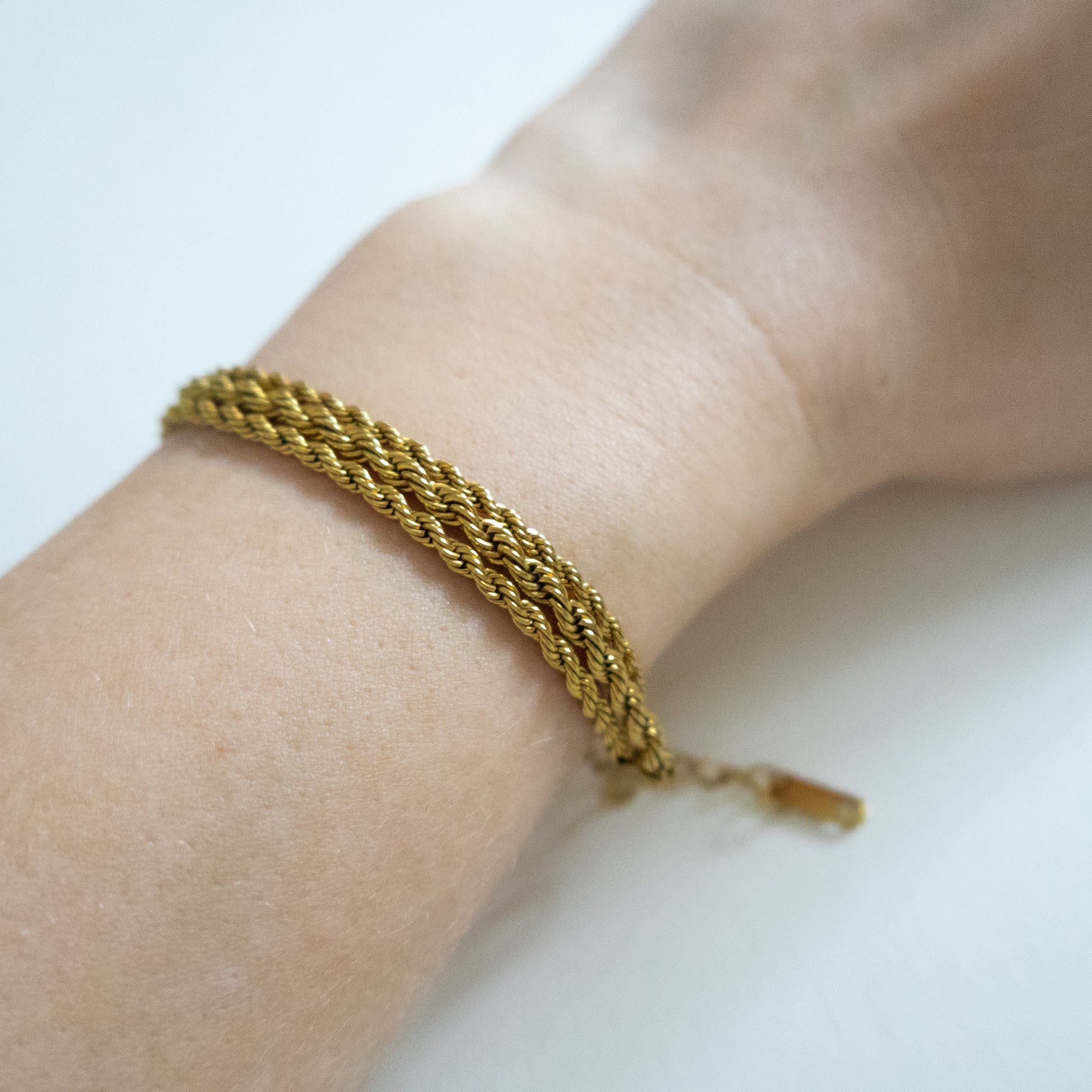 Gold braided bracelet on a wrist with a plain background