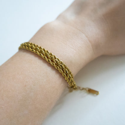 Gold braided bracelet on a wrist with a plain background