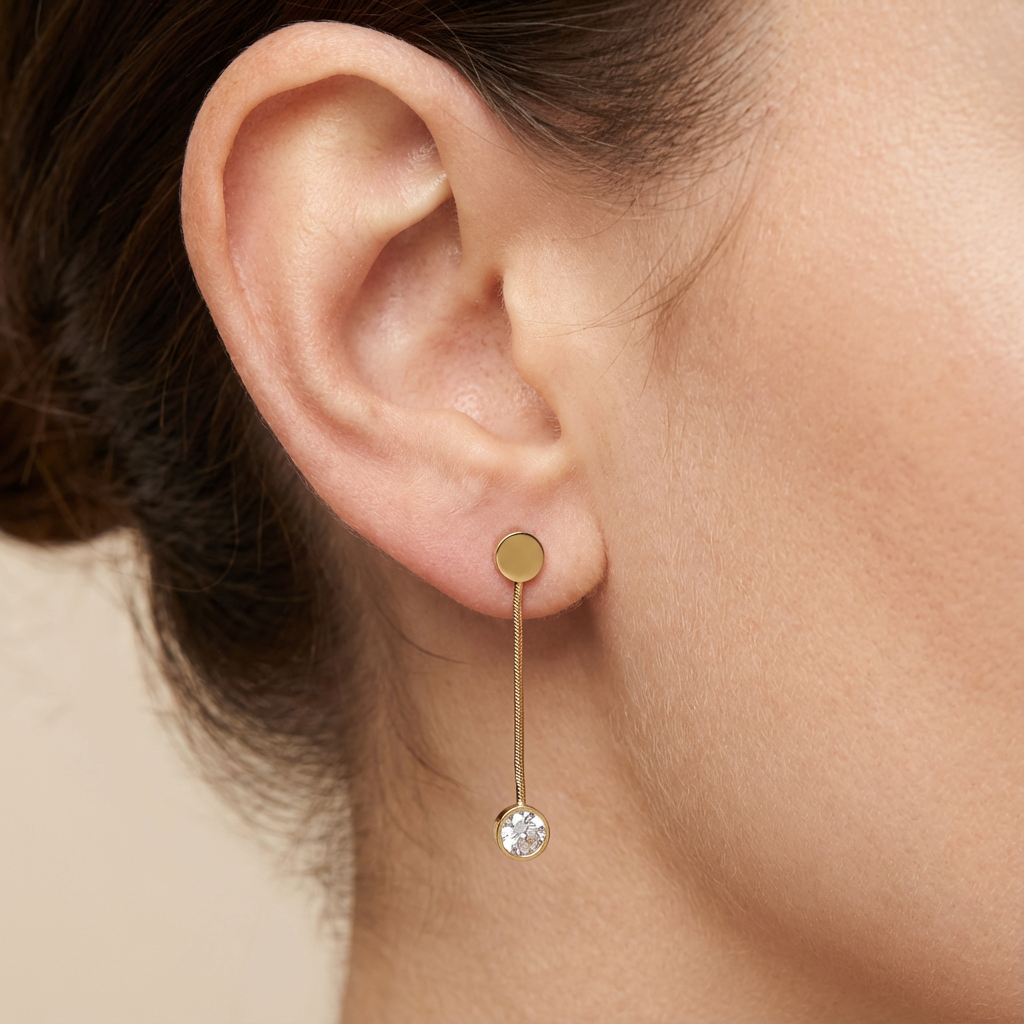 Gold earring with a small round gemstone worn by a person.