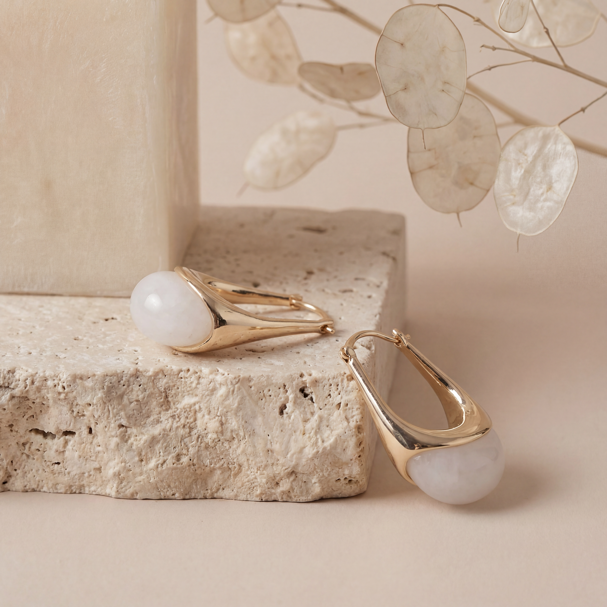 Gold earrings with white stones on a stone surface with decorative leaves in the background