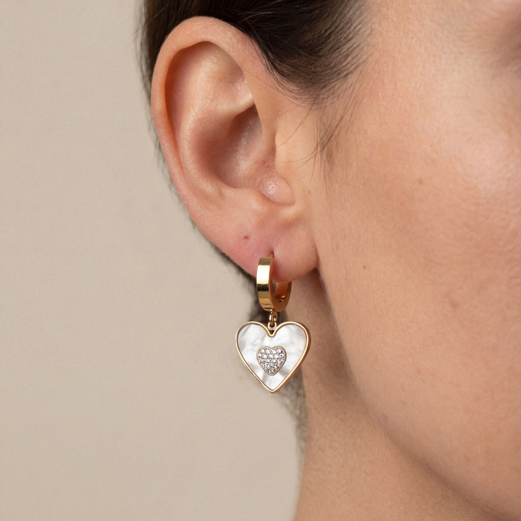 Gold heart-shaped earring worn by a person on a neutral background