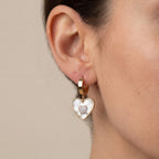 Gold heart-shaped earring worn by a person on a neutral background