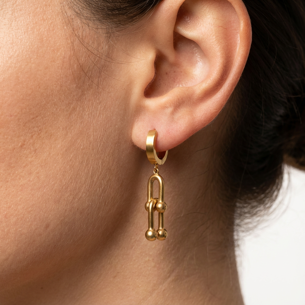 Gold hoop earring with a dangling charm worn by a person