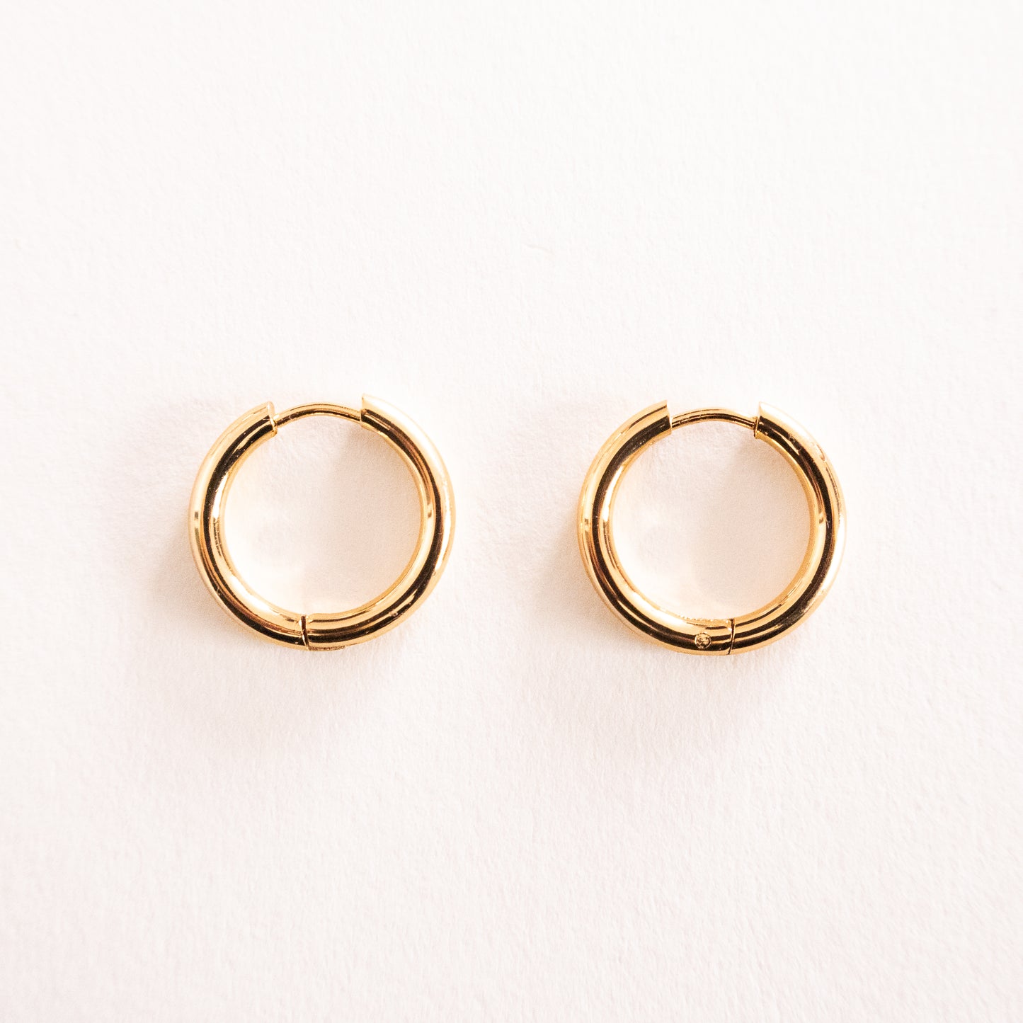 Gold hoop earrings on a light pink background