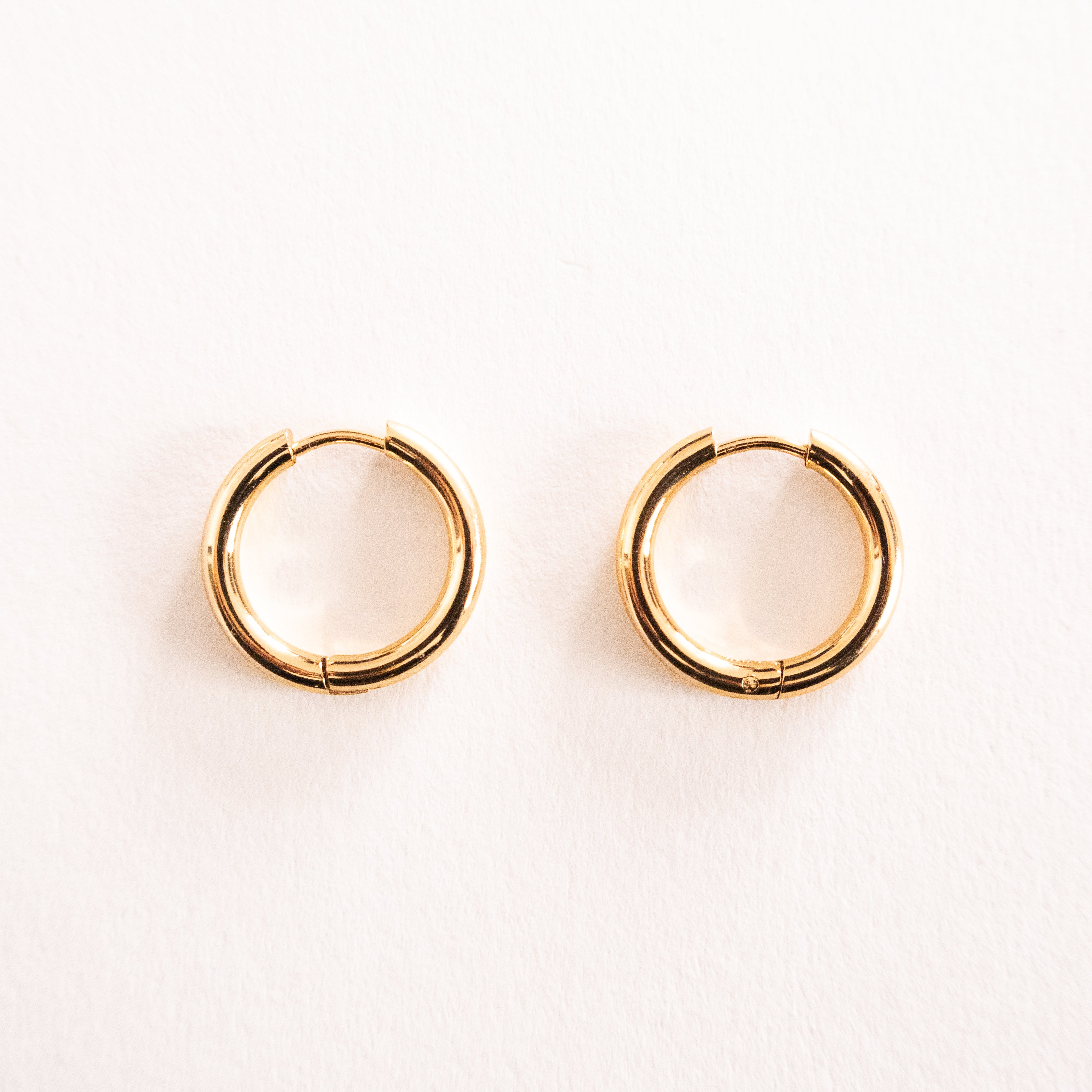 Gold hoop earrings on a light pink background