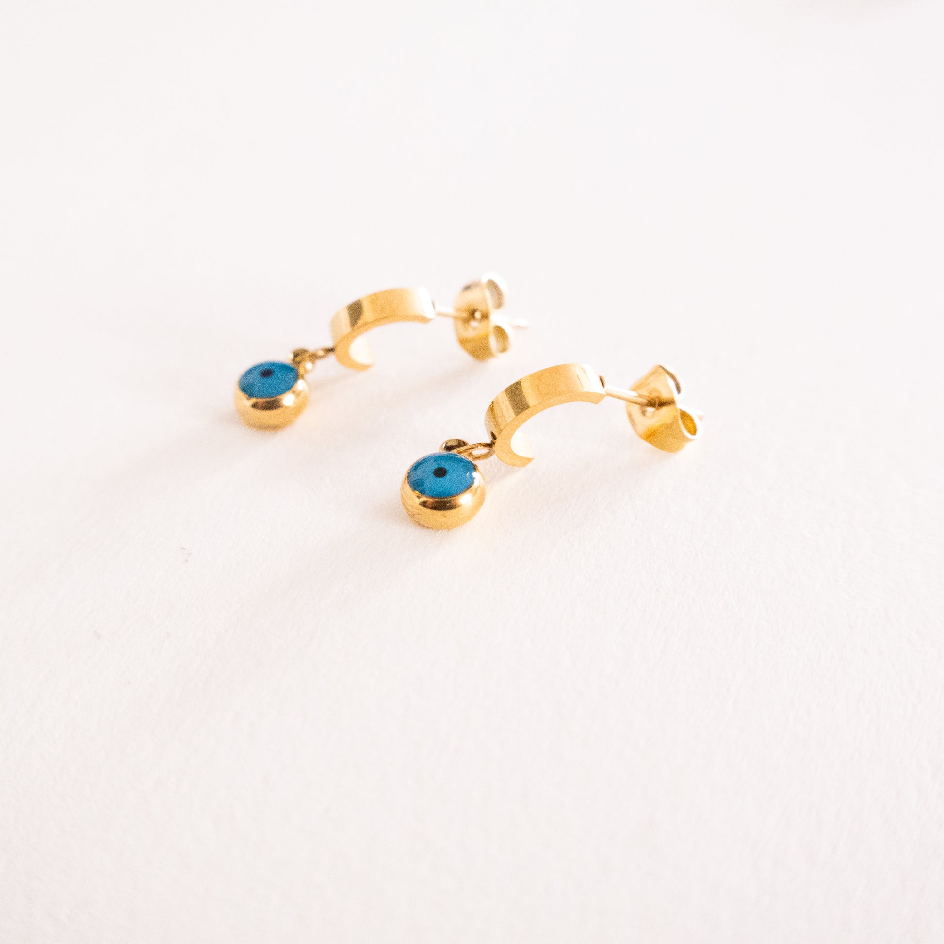 Gold hoop earrings with blue gemstones on a light gray background