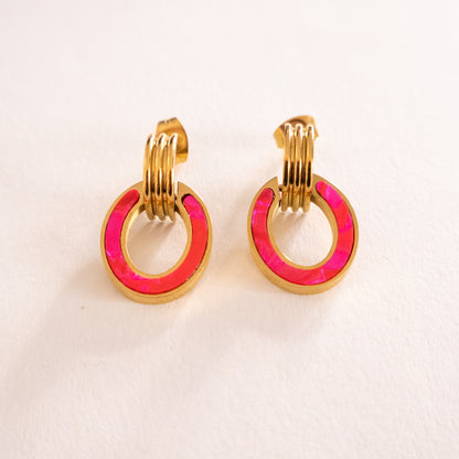 Gold hoop earrings with pink circular accents on a light pink background