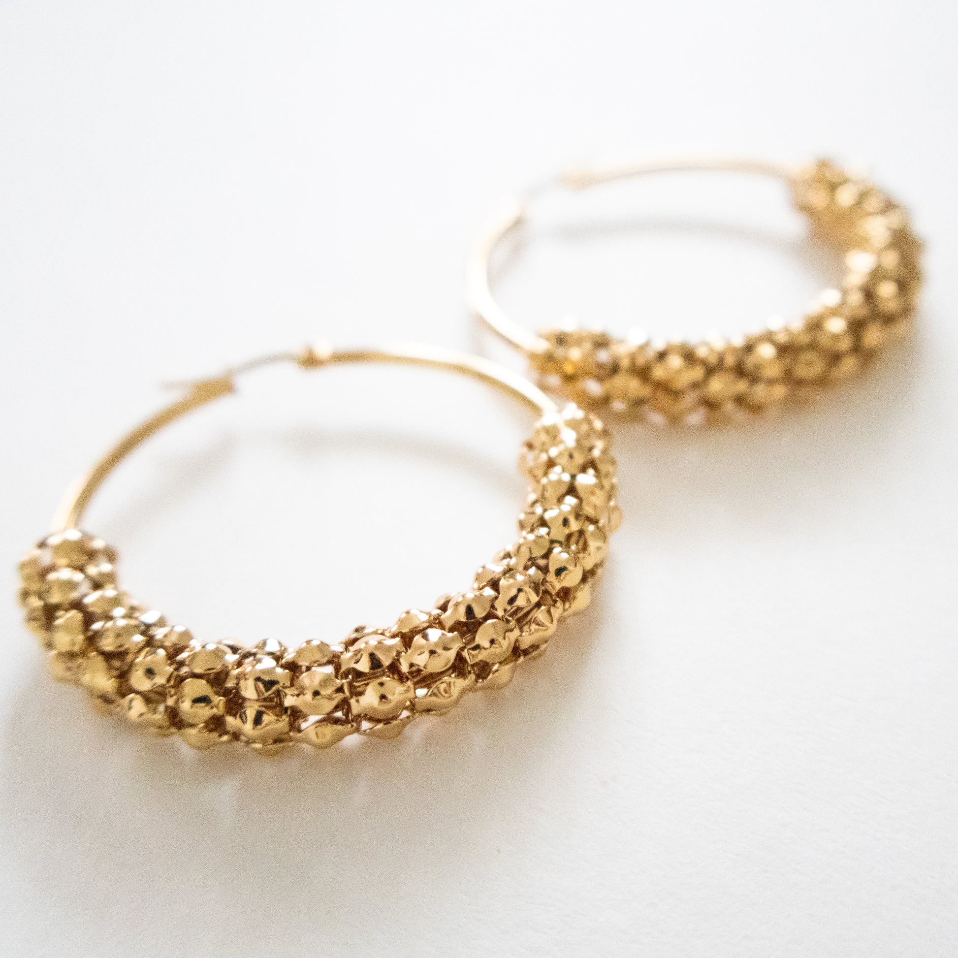 Gold hoop earrings with textured design on a white background