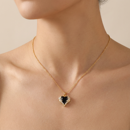Gold necklace with a heart-shaped pendant featuring a black center and white accents on a person's neck.