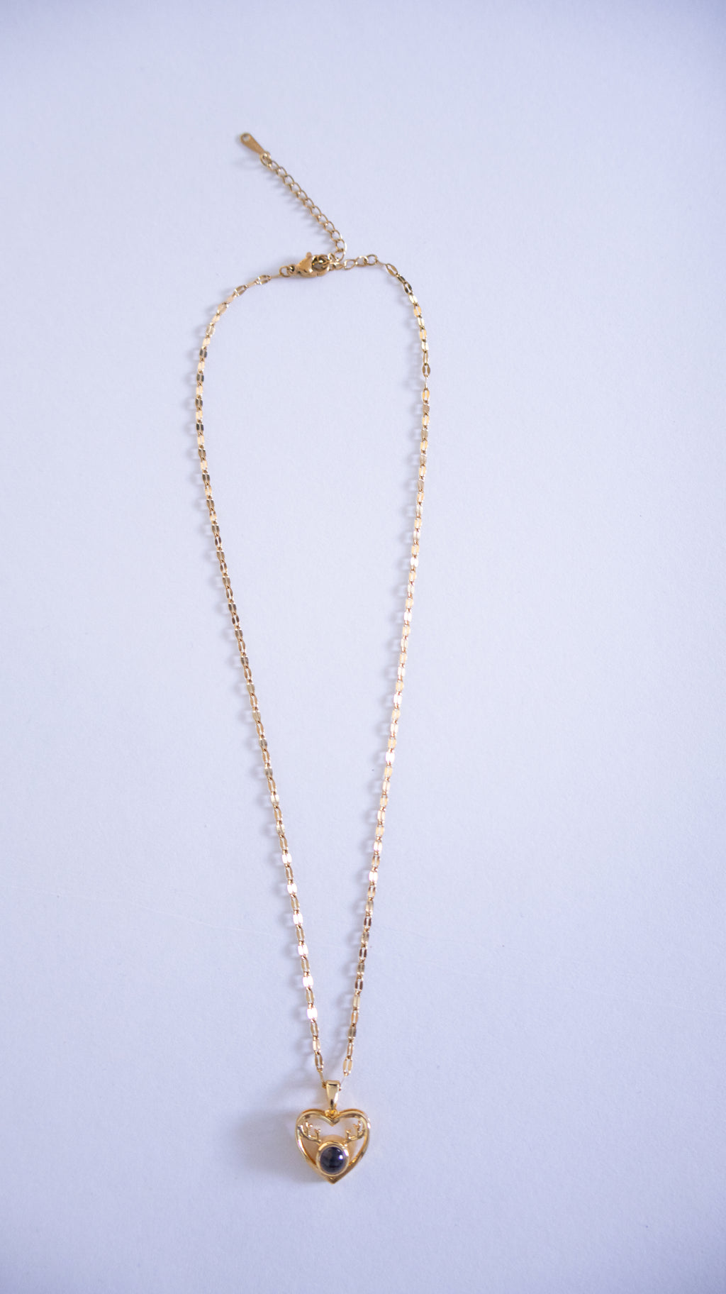 Gold necklace with a heart-shaped pendant on a light purple background