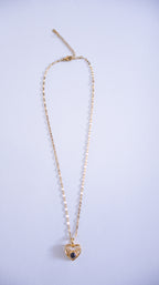 Gold necklace with a heart-shaped pendant on a light purple background