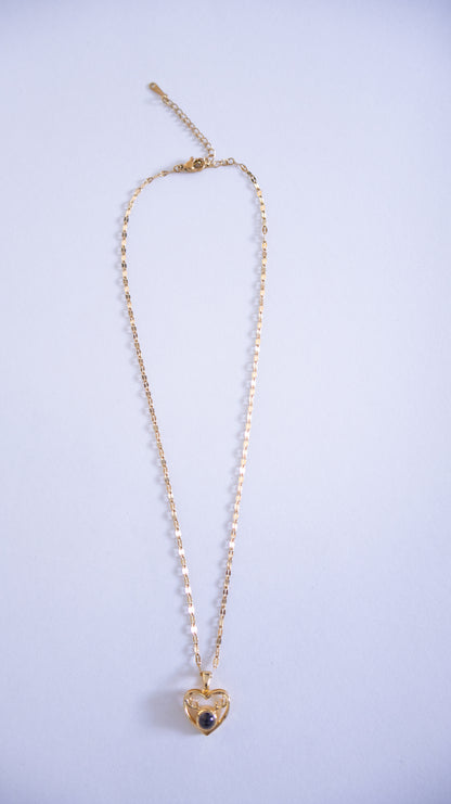 Gold necklace with a heart-shaped pendant on a light purple background