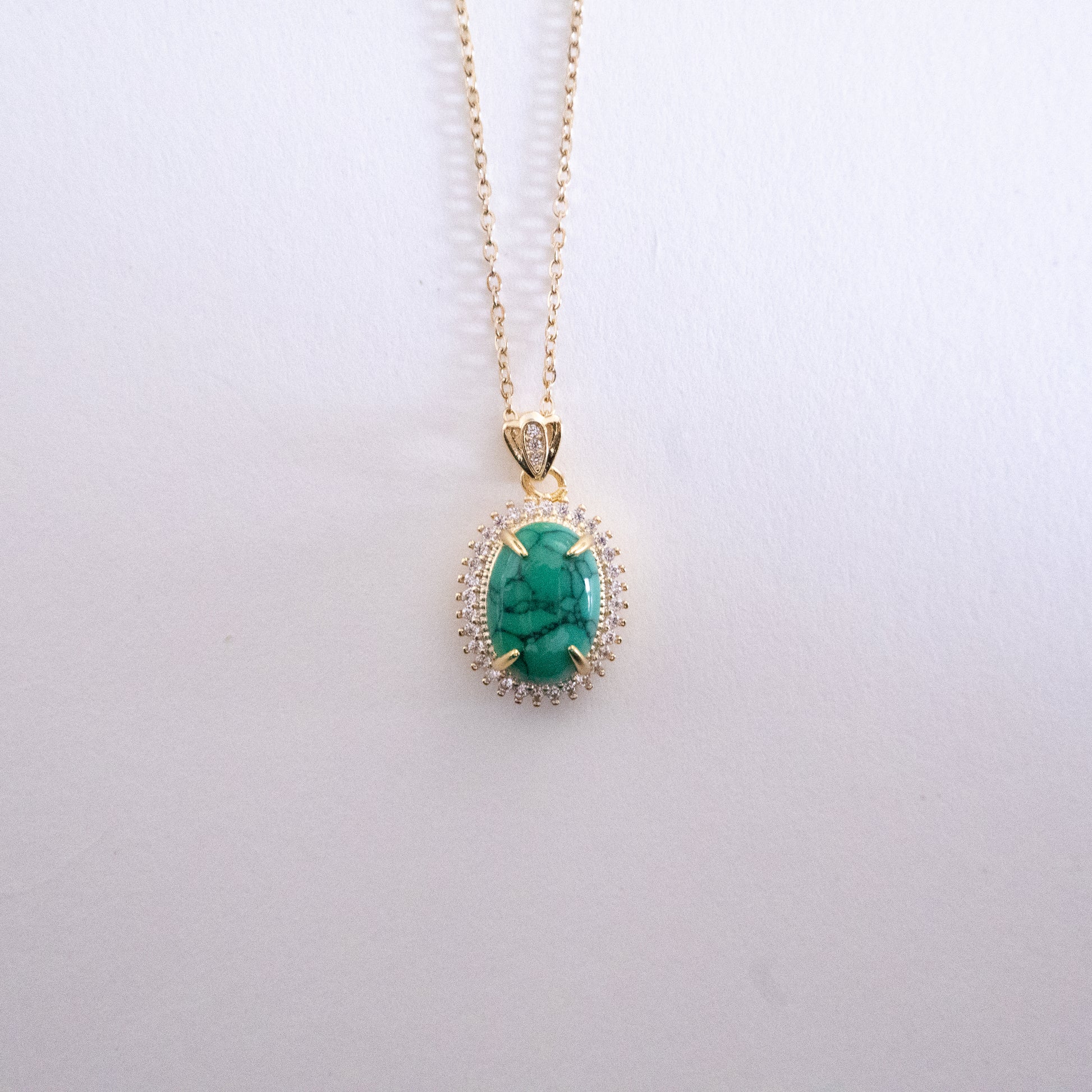 Gold necklace with a green gemstone pendant on a white background