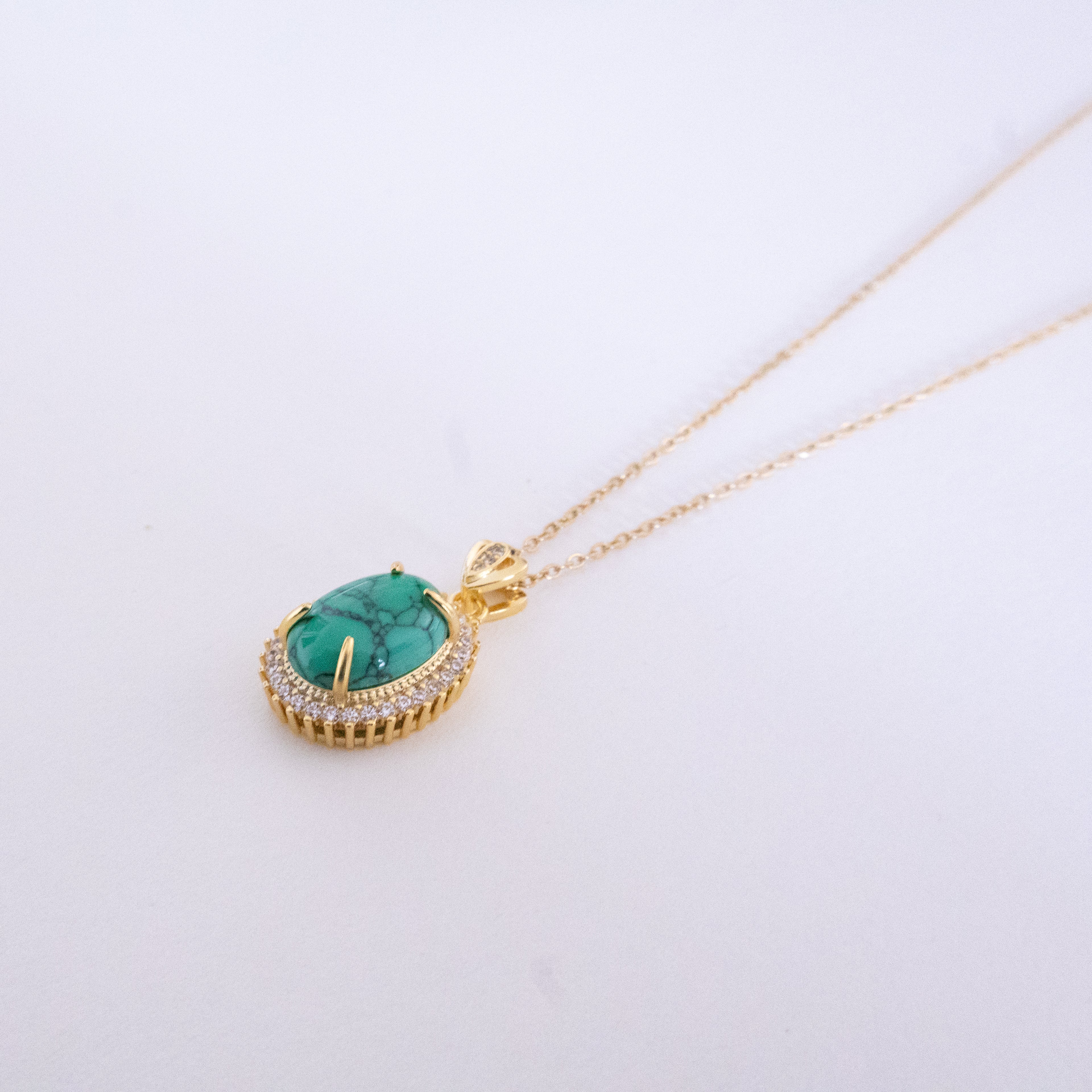 Gold necklace with a green gemstone pendant on a light gray background